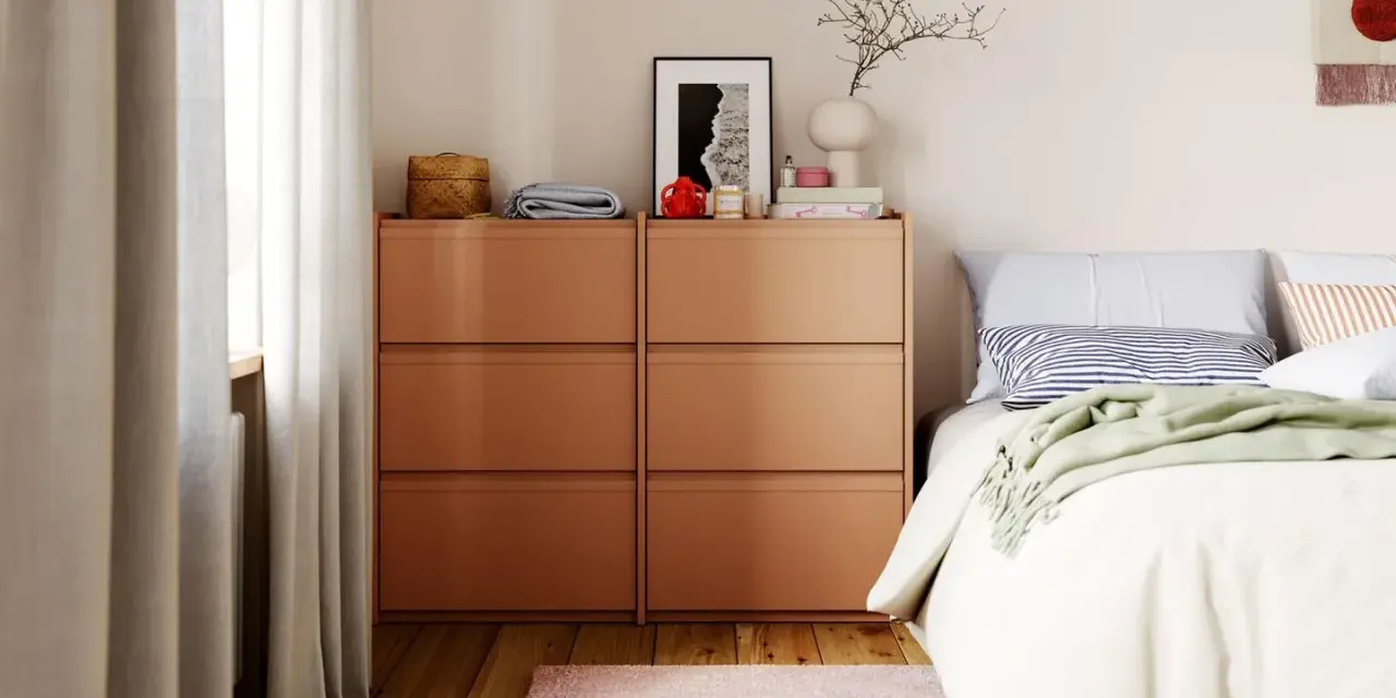 Moderne schlafzimmer ideen: Orange Kommoden neben einem Bett mit gestreifter Kissen und grüner Decke. Ein rosa Teppich und Hausschuhe liegen auf dem Holzboden.