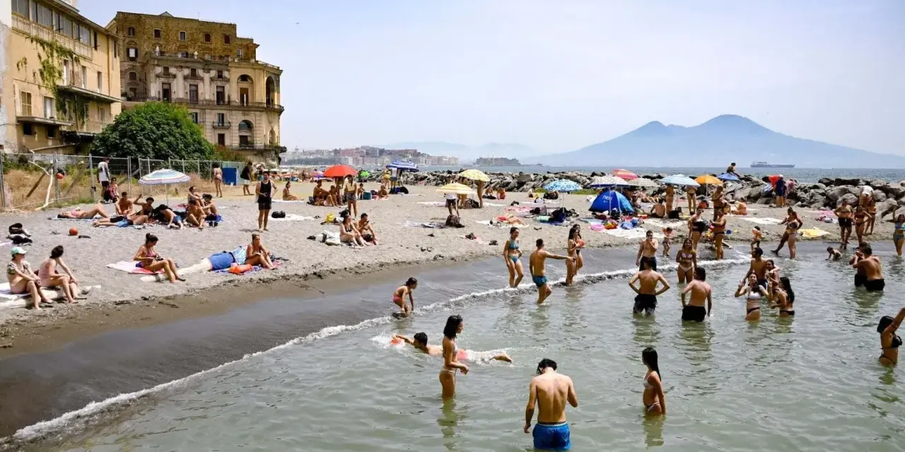 Gente che si gode il sole e il mare sulle spiagge libere di Napoli, con il Vesuvio sullo sfondo.