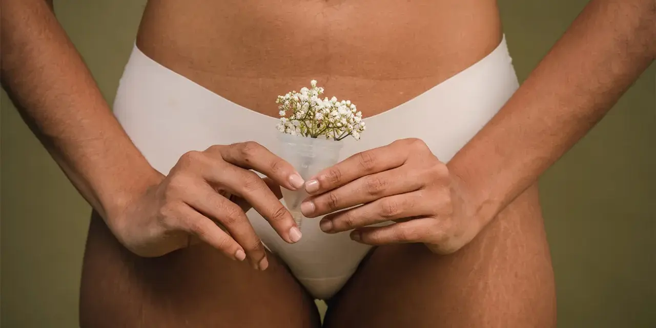 Kobieta trzyma kubeczek menstruacyjny z kwiatami, symbolizujący naturalność cyklu. To część odpowiedzi na pytanie: co to okres.