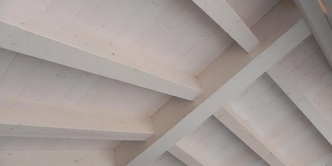Techo de madera con vigas y tablones, acabado con veladura blanca que resalta la veta natural.