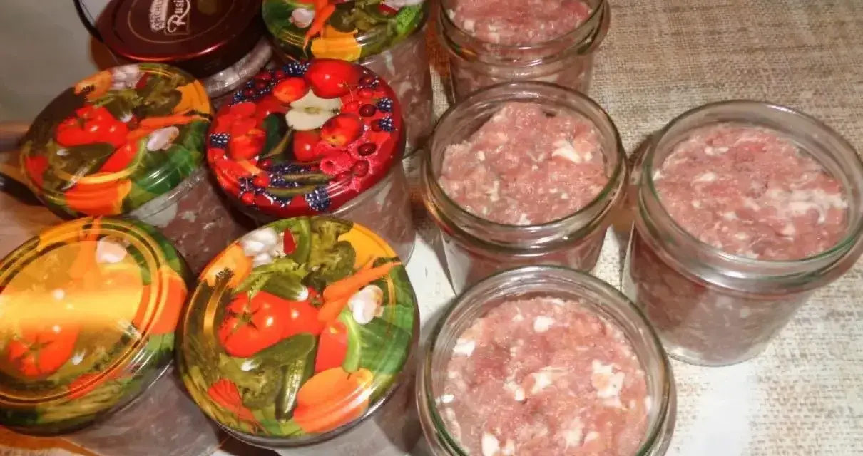 Słoiki z mielonym mięsem, gotowe do pasteryzacji. To pierwszy krok, jak zrobić kiełbasa w słoiku z galaretką. Kolorowe nakrętki z warzywami i owocami.