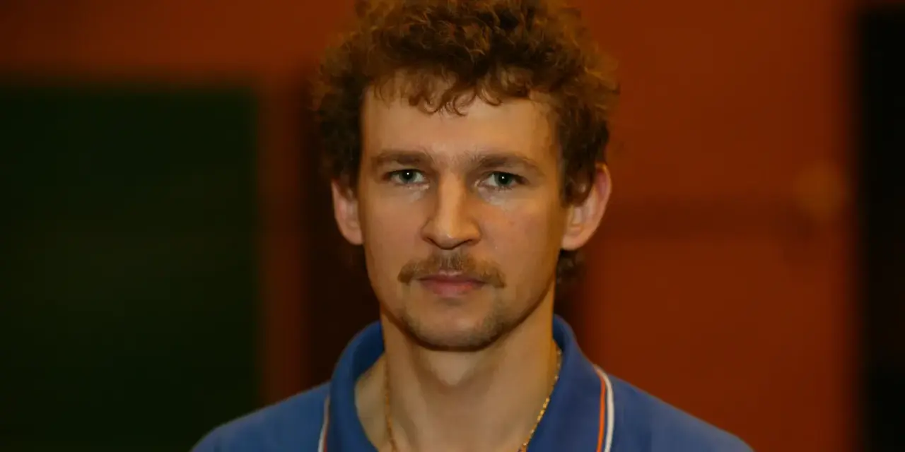 Tomasz Wronka, z kręconymi włosami i wąsami, w niebieskiej koszulce polo.