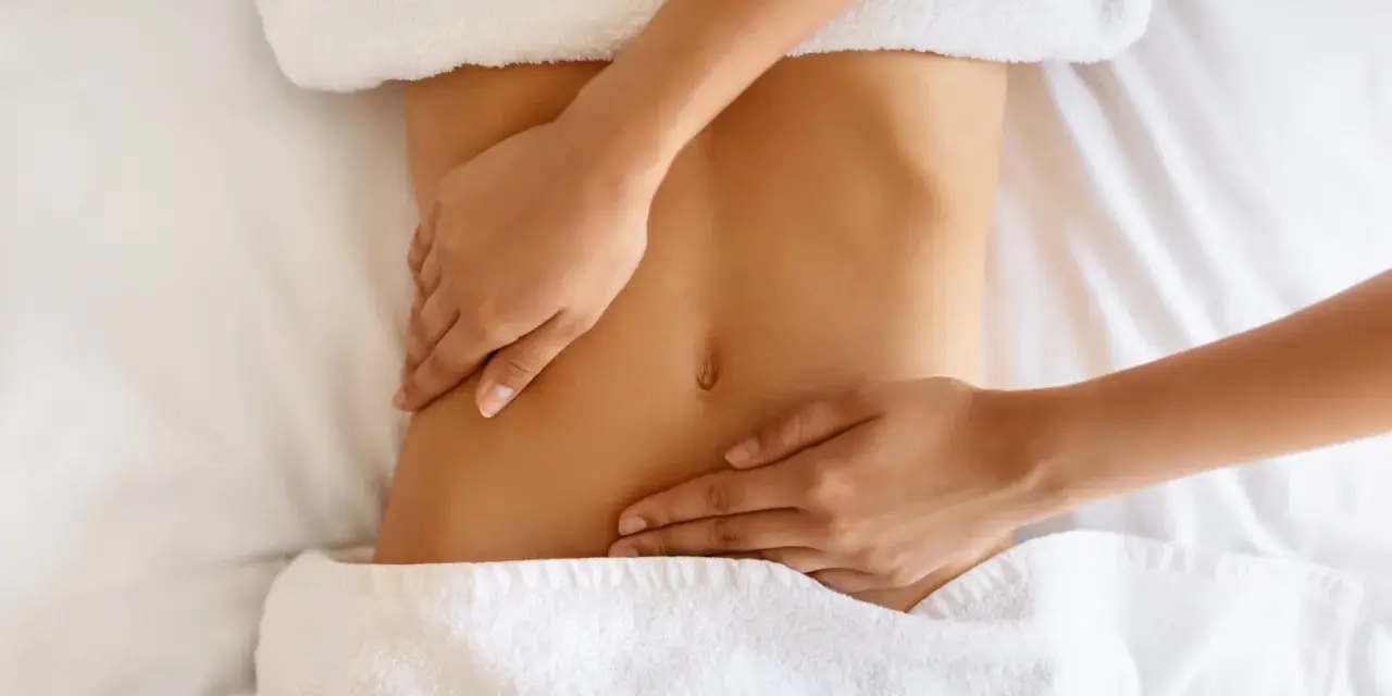 Hände massieren sanft den Bauch einer Frau. Manche empfinden Lymphdrainage als schmerzhaft, doch hier scheint es eine wohltuende Behandlung zu sein.