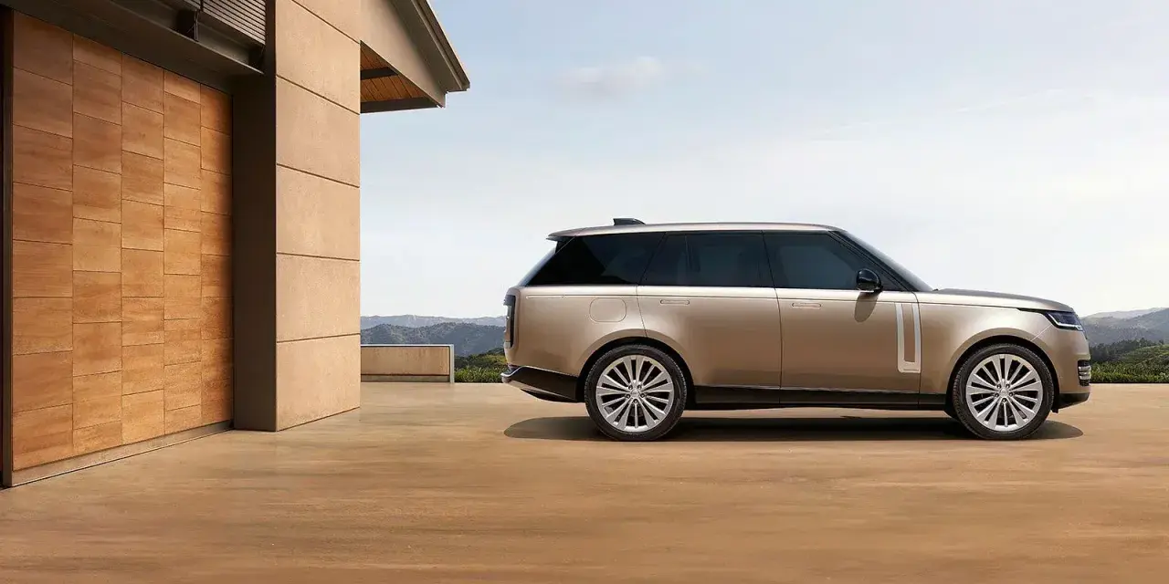 Elegancki Range Rover w kolorze piaskowym, zaparkowany przed nowoczesnym domem z drewnianymi drzwiami. Sprawdź range rover cena!