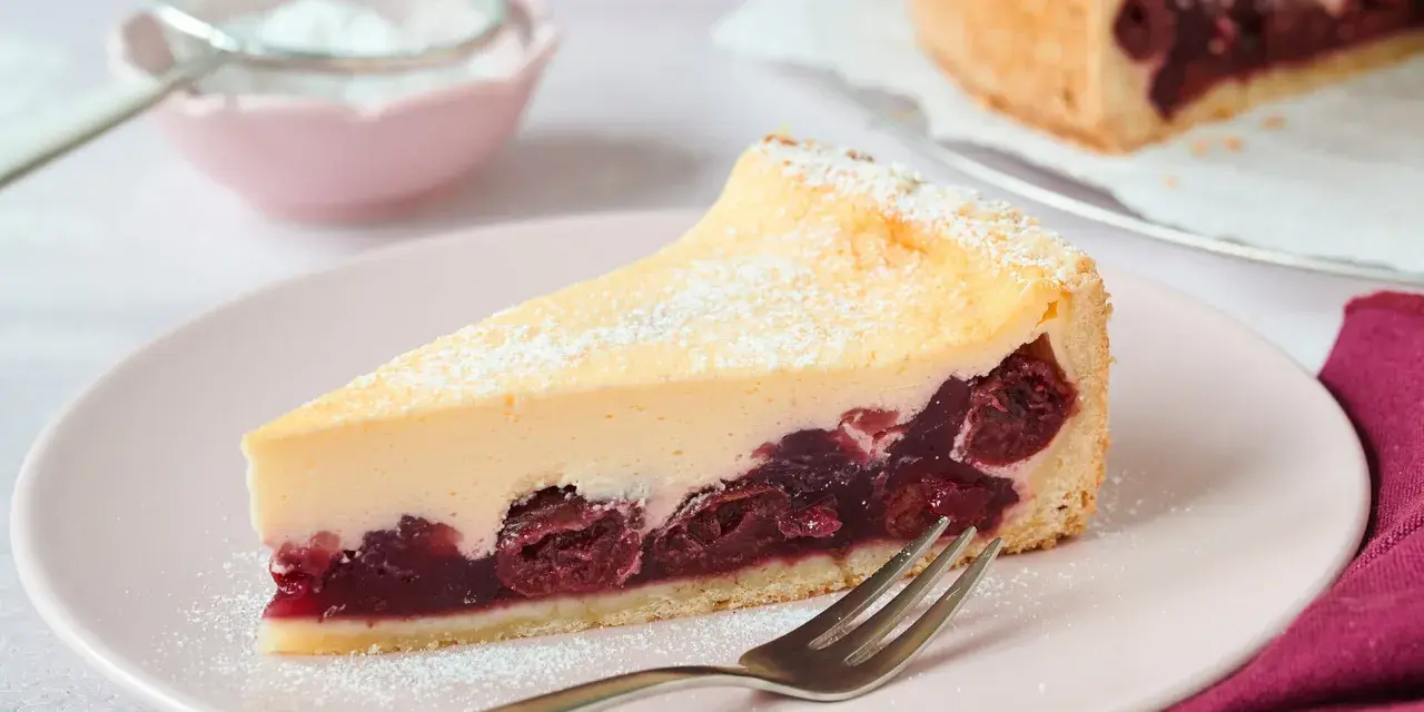 Ein saftiges Stück Kirsch Schmand Kuchen mit cremigem Belag und Kirschen auf Mürbeteigboden, bestäubt mit Puderzucker.