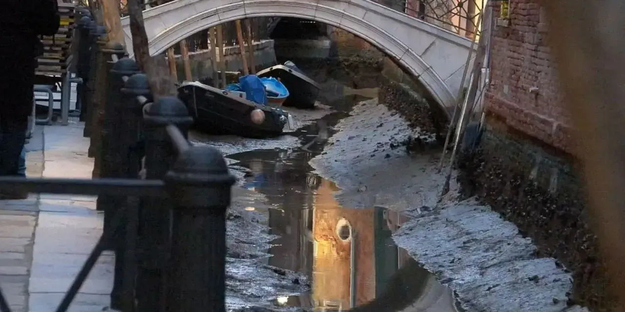 Canali di Venezia quasi asciutti, con barche arenate e riflessi di palazzi. Si vede quanto sono profondi i canali di Venezia in questa situazione insolita.