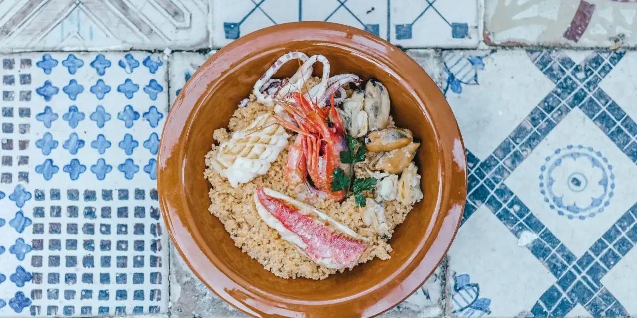 Un saporito cous cous di pesce con gamberi, calamari, cozze e triglia, guarnito con prezzemolo fresco.