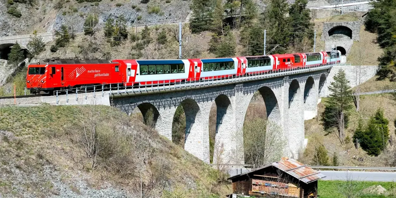 The red and white Glacier Express train travels across a stone viaduct, a scenic journey from Chur to Zermatt.