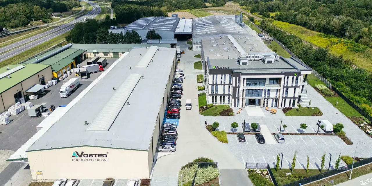 Nowoczesny kompleks produkcyjny Voster producent drzwi, z drogą szybkiego ruchu w tle.