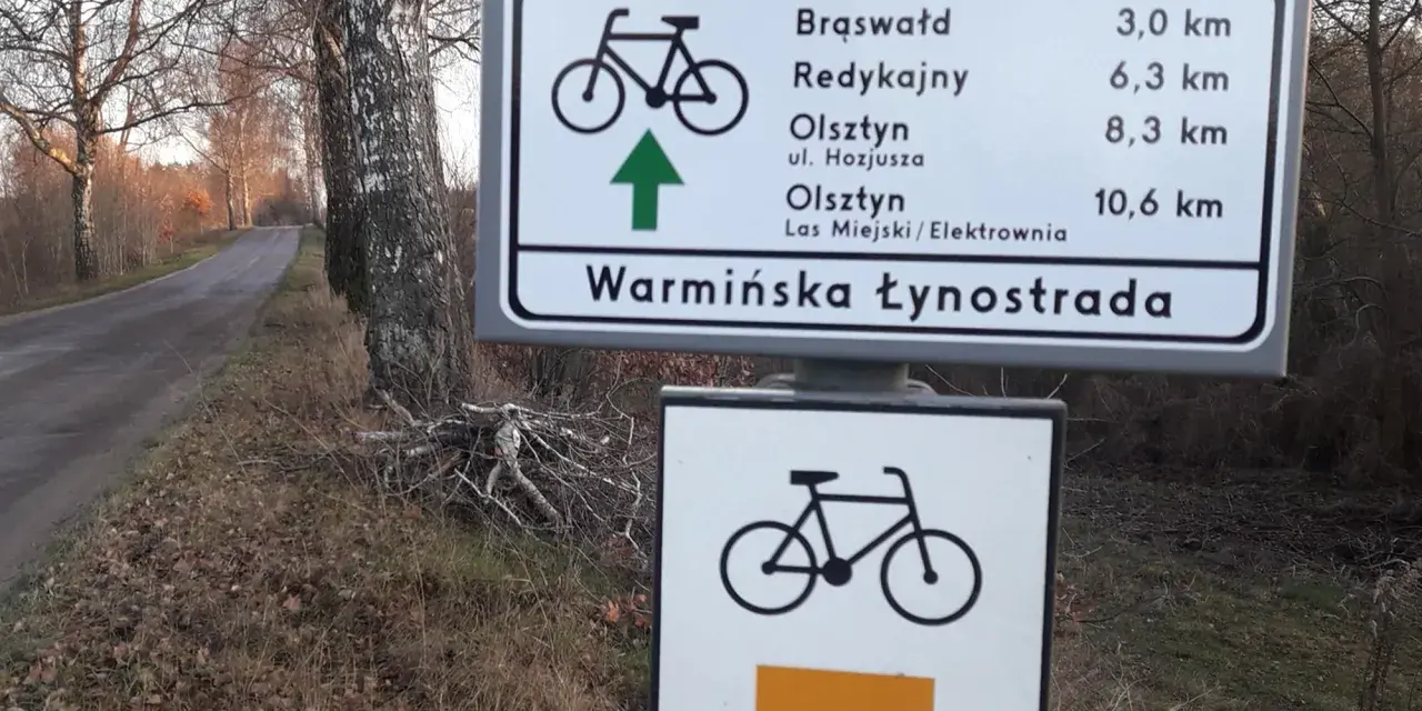 Znak drogowy informuje o odległościach do Brąswałd, Redykajn, Olsztyna i Lasu Miejskiego. To część szlaku Warmińska Łynostrada.