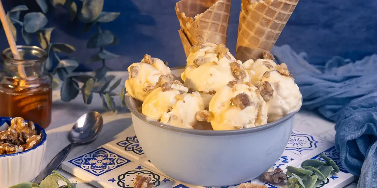Schüssel mit Eiscreme, garniert mit Nüssen und Honig. Ein Glas Honig und Waffelhörnchen im Hintergrund. Ein süßer Genuss: Eis mit Honig statt Zucker.