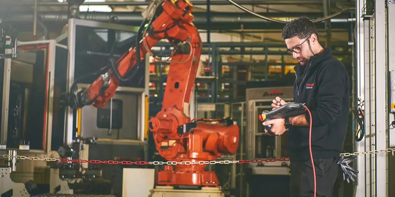 Un tecnico controlla un braccio robotico rosso in una fabbrica, dimostrando la meccatronica cos'è: l'integrazione di meccanica, elettronica e informatica.