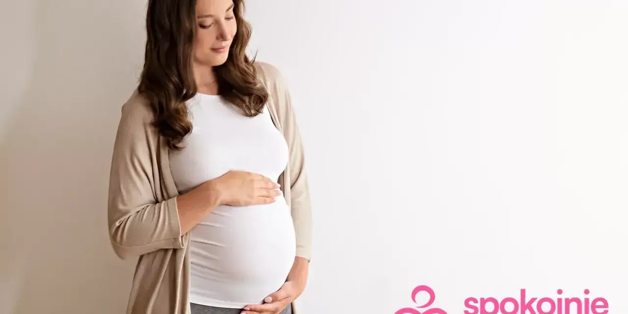 Kobieta w 29 tygodniu ciąży, z dłońmi na brzuchu, patrzy z miłością na swoje dziecko.