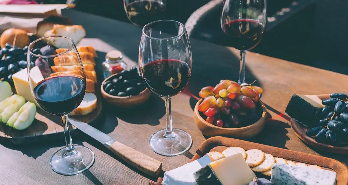 Degustacja wina merlot: jakie to wino? Kieliszki pełne rubinowego trunku, deska serów, winogrona, oliwki i figi tworzą idealną kompozycję.