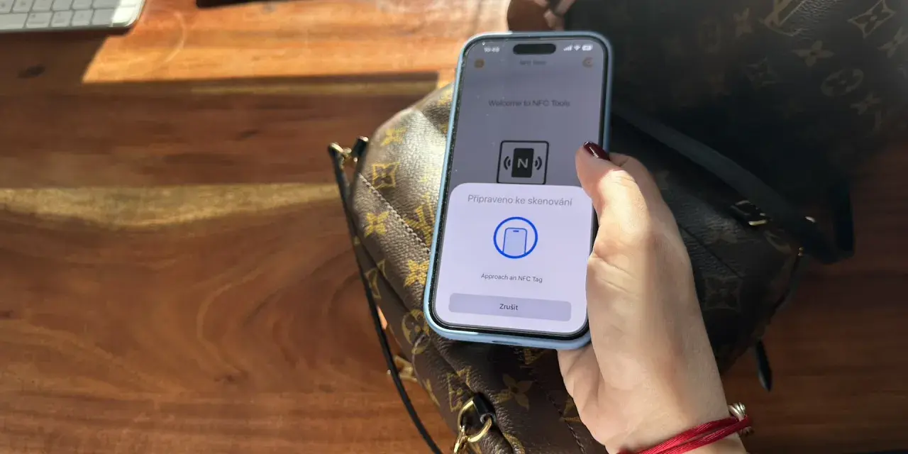 Dłoń trzymająca telefon z aplikacją NFC nad torebką Louis Vuitton.
