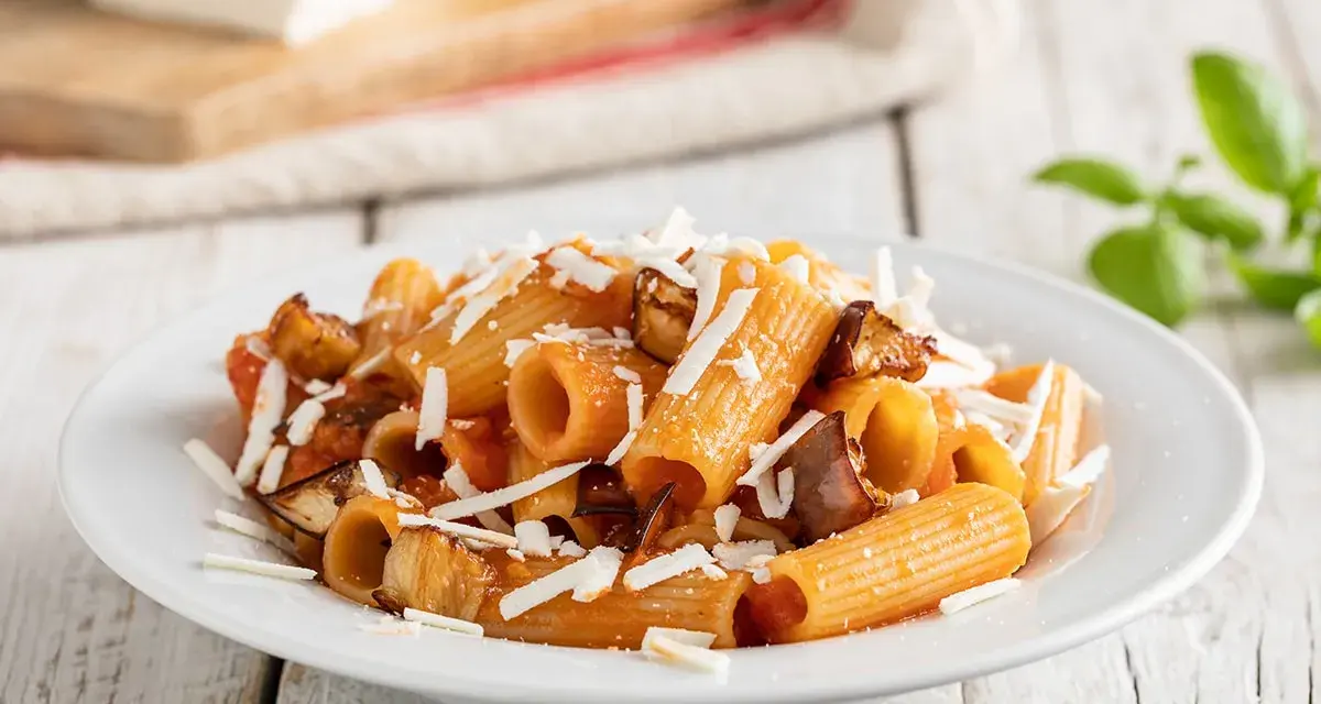Piatto di pasta alla norma con rigatoni, melanzane fritte, pomodoro e ricotta salata grattugiata.