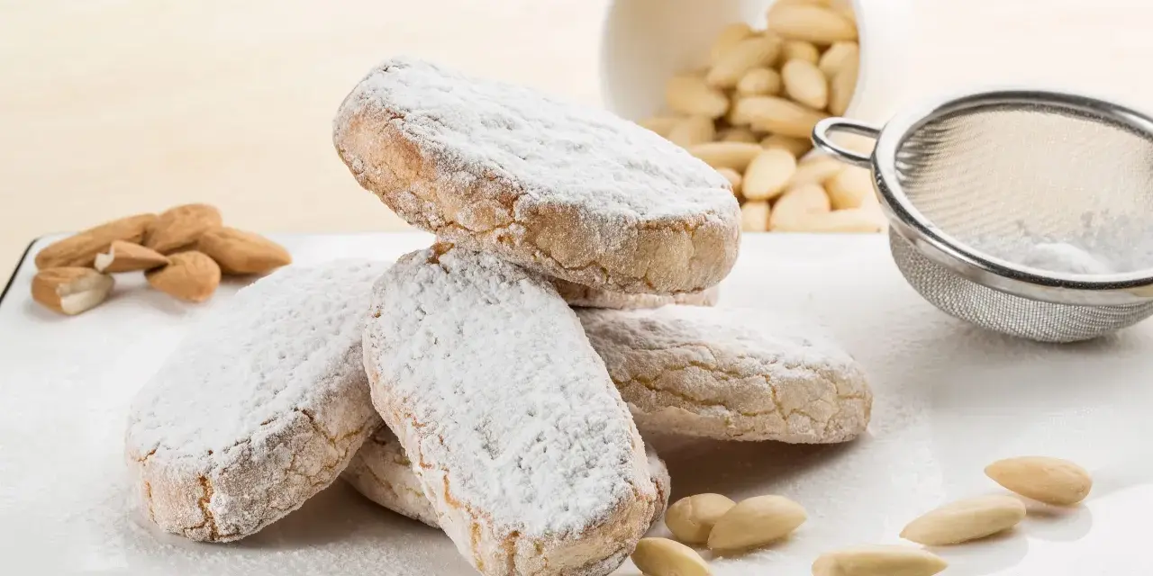 Dolce di Siena cosparso di zucchero a velo, con mandorle e setaccio sullo sfondo.