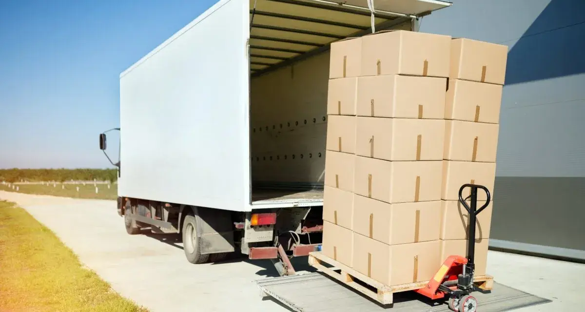 Stos kartonów na palecie, gotowy do załadunku do białej ciężarówki. Ubezpieczenia cargo chronią takie przesyłki.