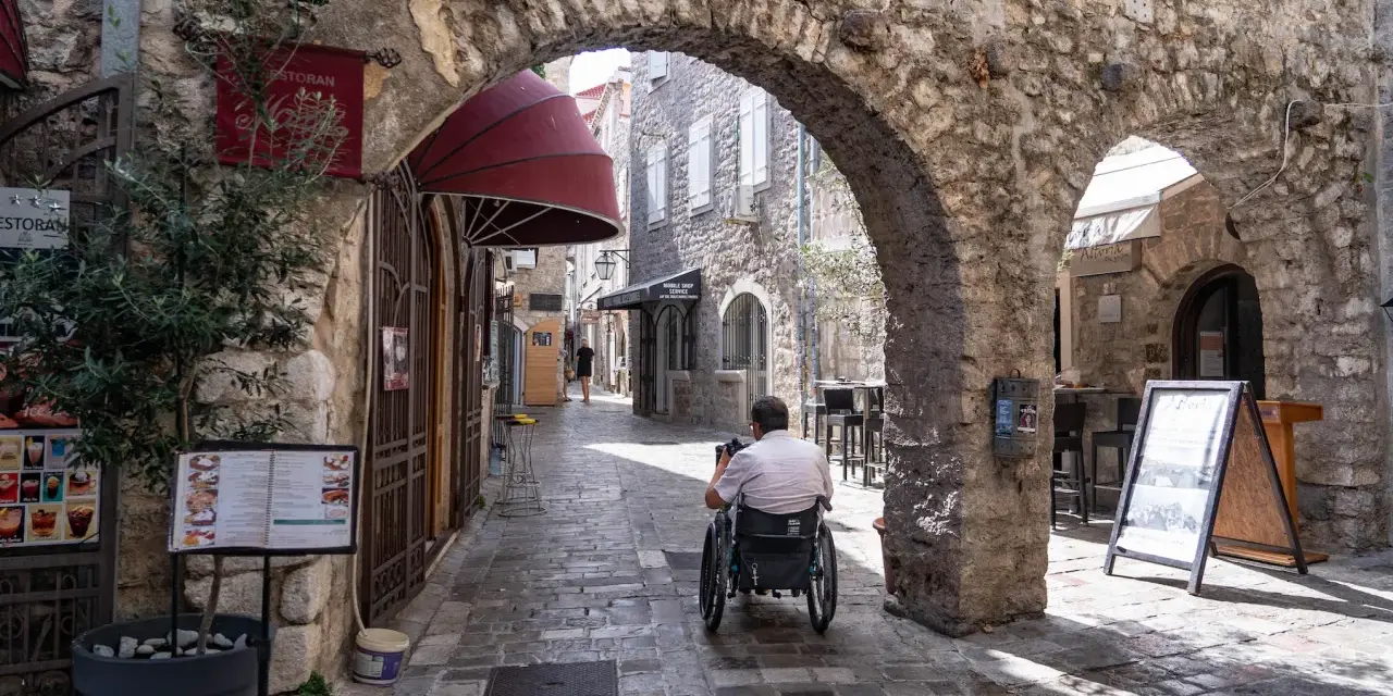 Mężczyzna na wózku inwalidzkim przemierza urokliwe, kamienne uliczki **Budva stare miasto**.