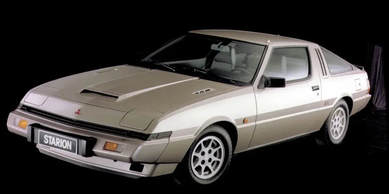 Klasyczny Mitsubishi Starion w kolorze szampańskim, z charakterystycznym wlotem powietrza na masce i sportowym nadwoziem coupe.