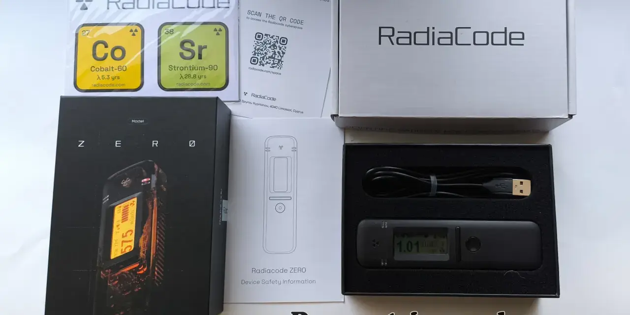 Zestaw Radiacode z dozymetrem ZERO, instrukcją i kablem USB. Obok pudełka z urządzeniem znajduje się karta z informacjami o izotopach Co-60 i Sr-90.