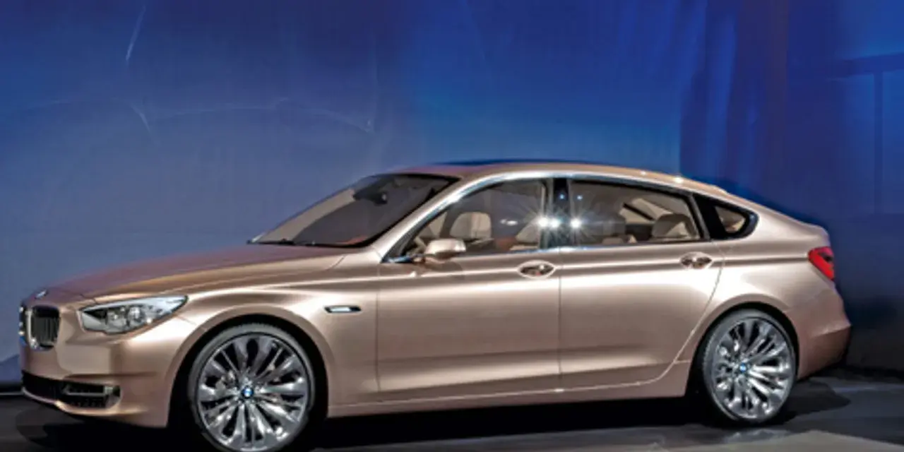 Eleganckie, złote bmw gt z przyciemnianymi szybami i chromowanymi felgami stoi na tle niebieskiej ściany.