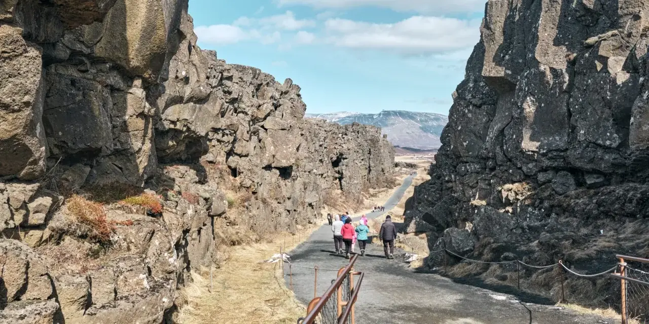 Spacerem przez szczelinę tektoniczną w parku narodowym Þingvellir. Grupa turystów podziwia surowe piękno islandzkiej przyrody.