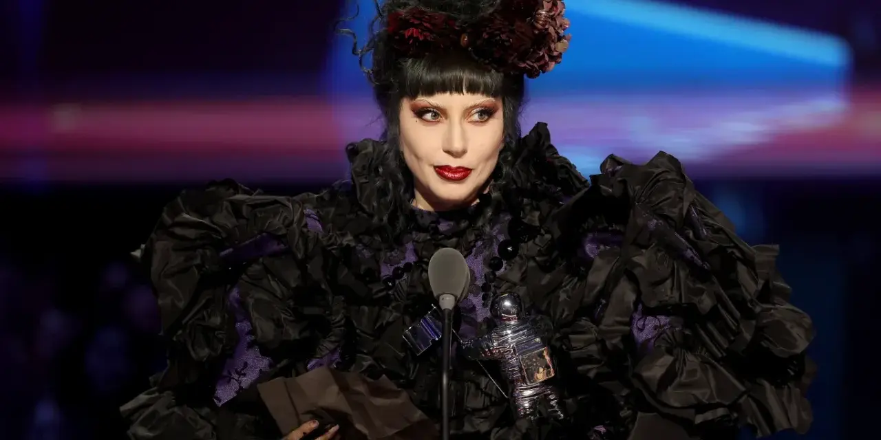 Lady Gaga w Polsce, w czarnej, falbaniastej sukni z fioletowymi wstawkami, odbiera nagrodę.