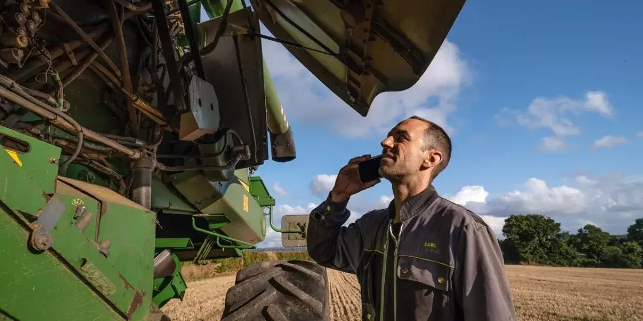 Rolnik rozmawia przez telefon, sprawdzając **waryński części** kombajnu.