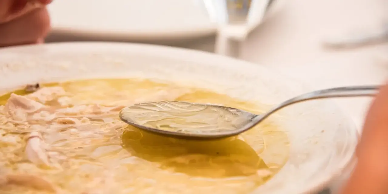 Caldo de pollo casero en un plato blanco con una cuchara.