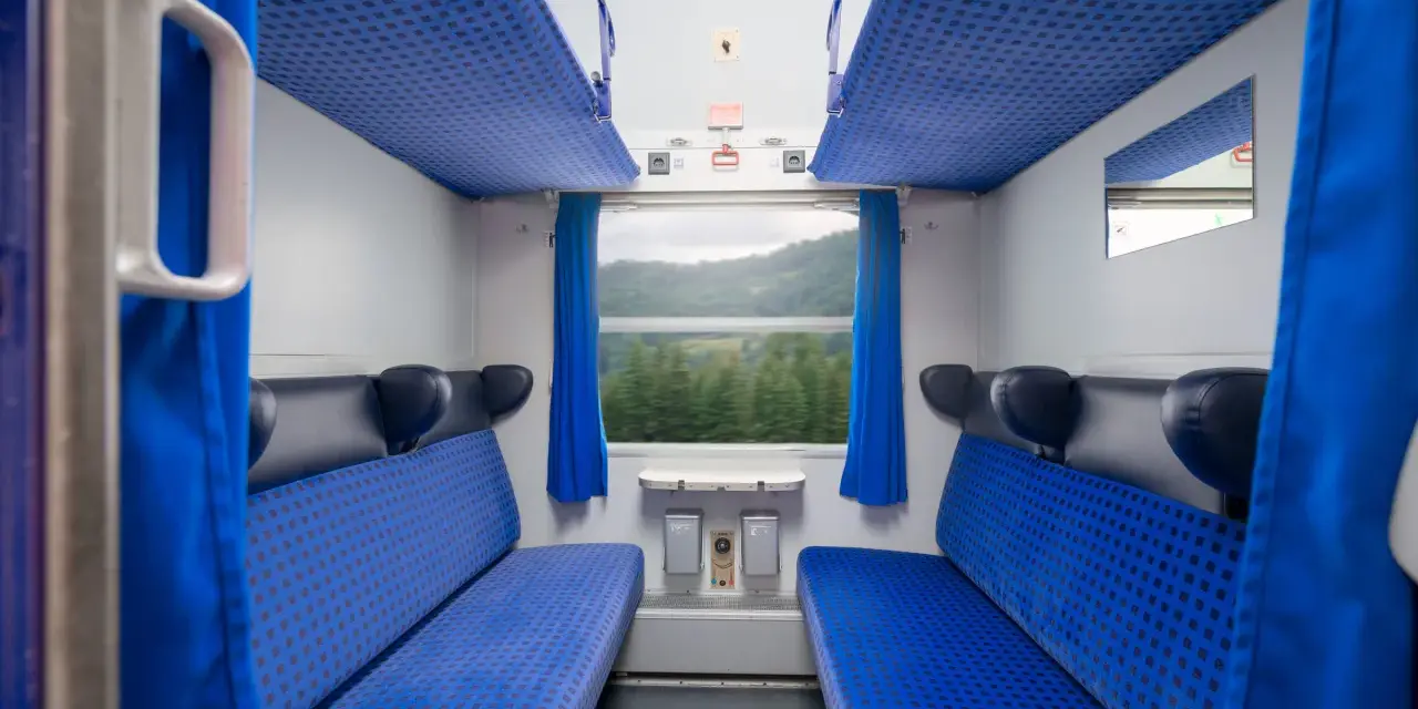 Wnętrze wagonu kolejowego z niebieskimi siedzeniami i zasłonami. Widok przez okno na zielone wzgórza. Idealne miejsce na podróż pociągiem do Berlina.