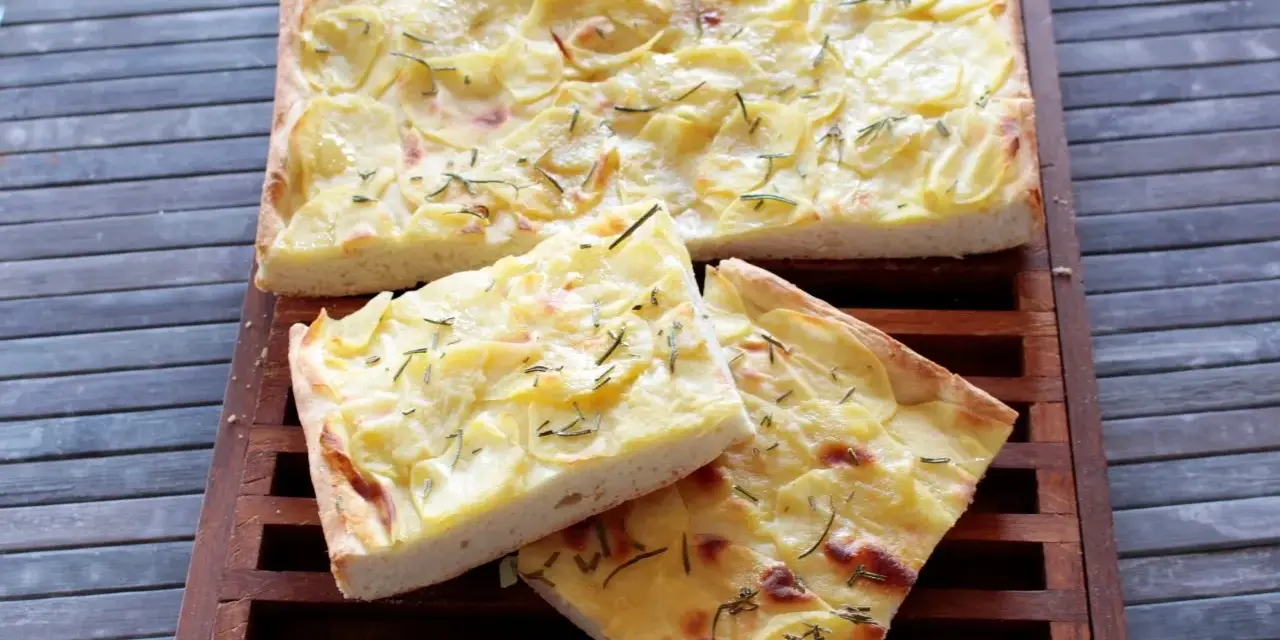 Focaccia con lievito istantaneo, ricca di patate e rosmarino, servita su un tagliere di legno.