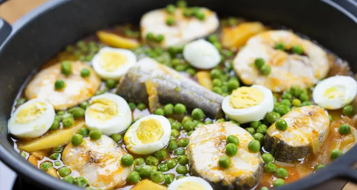 Merluza con guisantes y huevos duros en una sartén. Un plato casero y reconfortante.