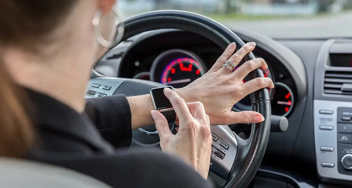 Frau tippt auf ihre Smartwatch am Steuer. Handy am Steuer Strafe vermeiden!