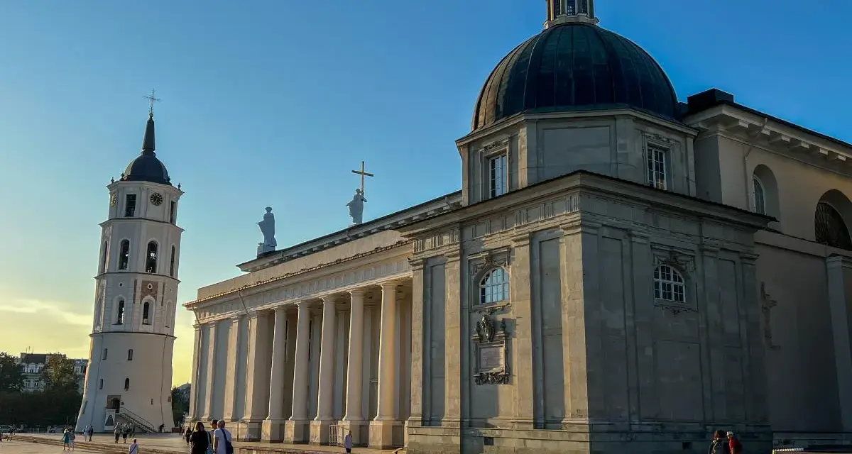 Wileńskie kościoły: Katedra i dzwonnica na placu. Słońce oświetla monumentalną architekturę, tworząc długie cienie.