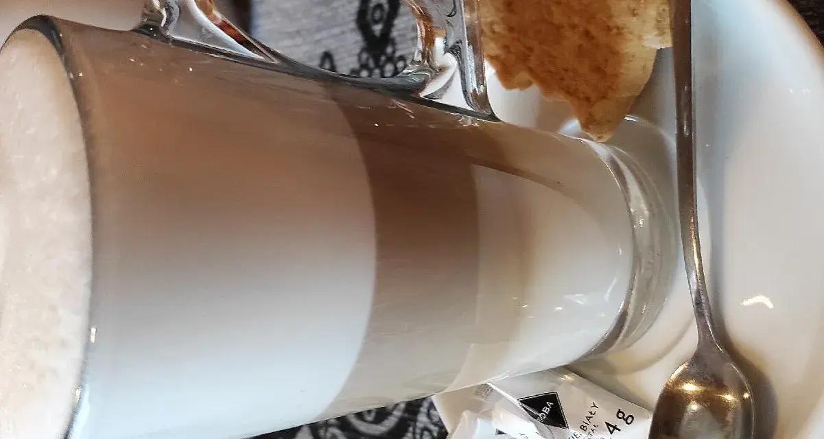 Kawa latte w szklance, obok ciasteczko i cukier. Idealna na przerwę w karczmie u wróbla menu.