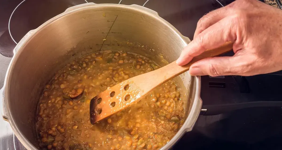 Lentejas deliciosas cocinándose en olla express, removidas con cuchara de madera.