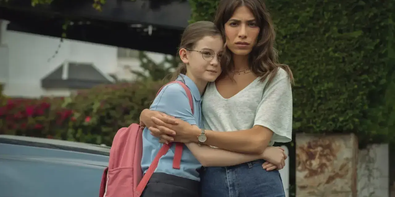 Erin Carter abbraccia una bambina con uno zaino rosa. La donna sembra preoccupata, la bambina protetta.