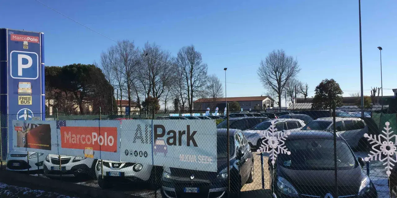 Parcheggio vicino all'aeroporto di Venezia Treviso con cartelli Marco Polo e All Park. Auto parcheggiate sotto un cielo azzurro.