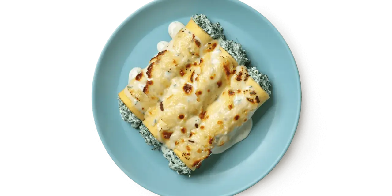 Tre cannelloni ripieni di ricotta e spinaci, gratinati al forno con besciamella e formaggio fuso, serviti su un piatto azzurro.
