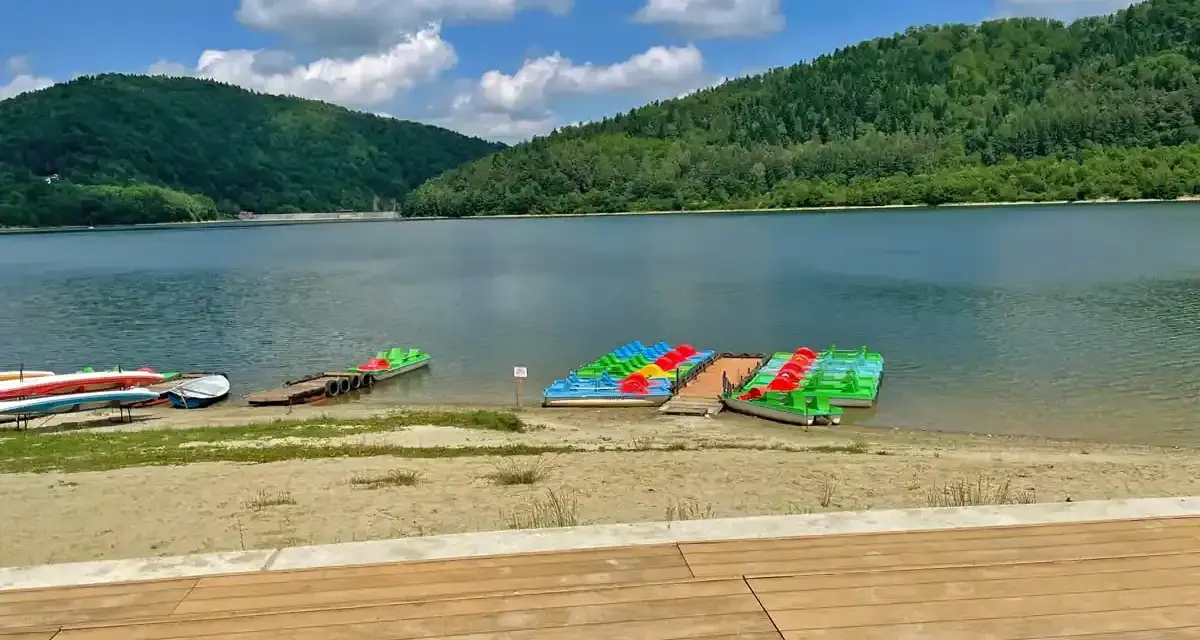 Kolorowe rowery wodne i kajaki czekają na plaży nad górskim jeziorem.