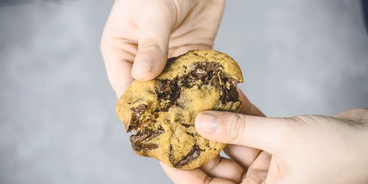 Hände halten einen frisch gebackenen American Cookie mit geschmolzener Schokolade. Perfekt zum amerikanischen Cookies backen!