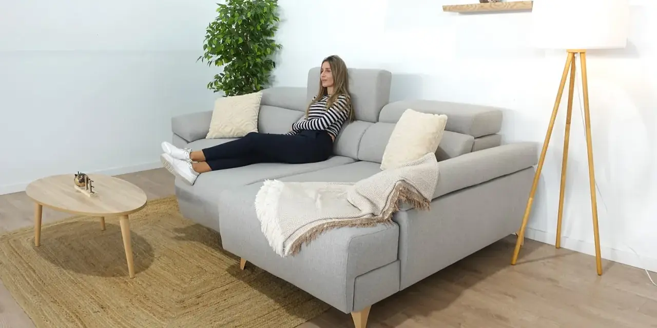 Mujer relajada en un sofá en medio del salón, con una manta y cojines.