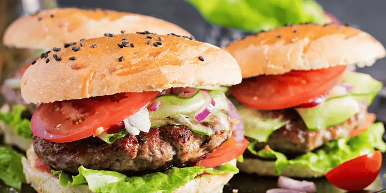 Dwa soczyste burgery wołowe z bułką, pomidorem, sałatą i ogórkiem.