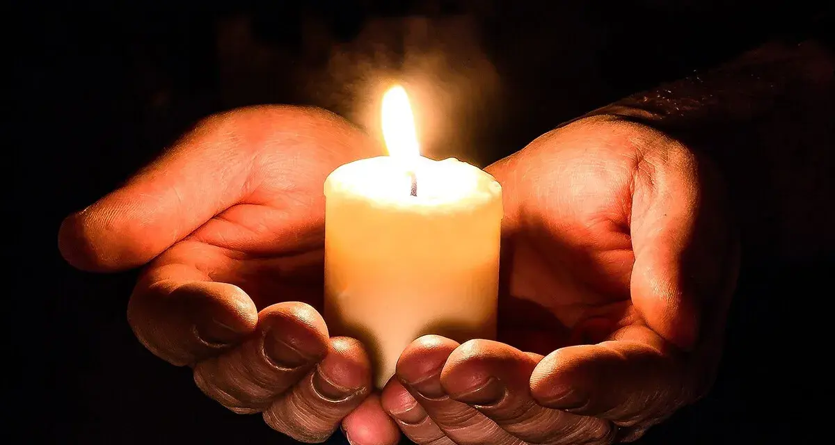 Hände halten eine brennende Kerze, ein Symbol für den Totensonntag, das Licht und Erinnerung spendet.
