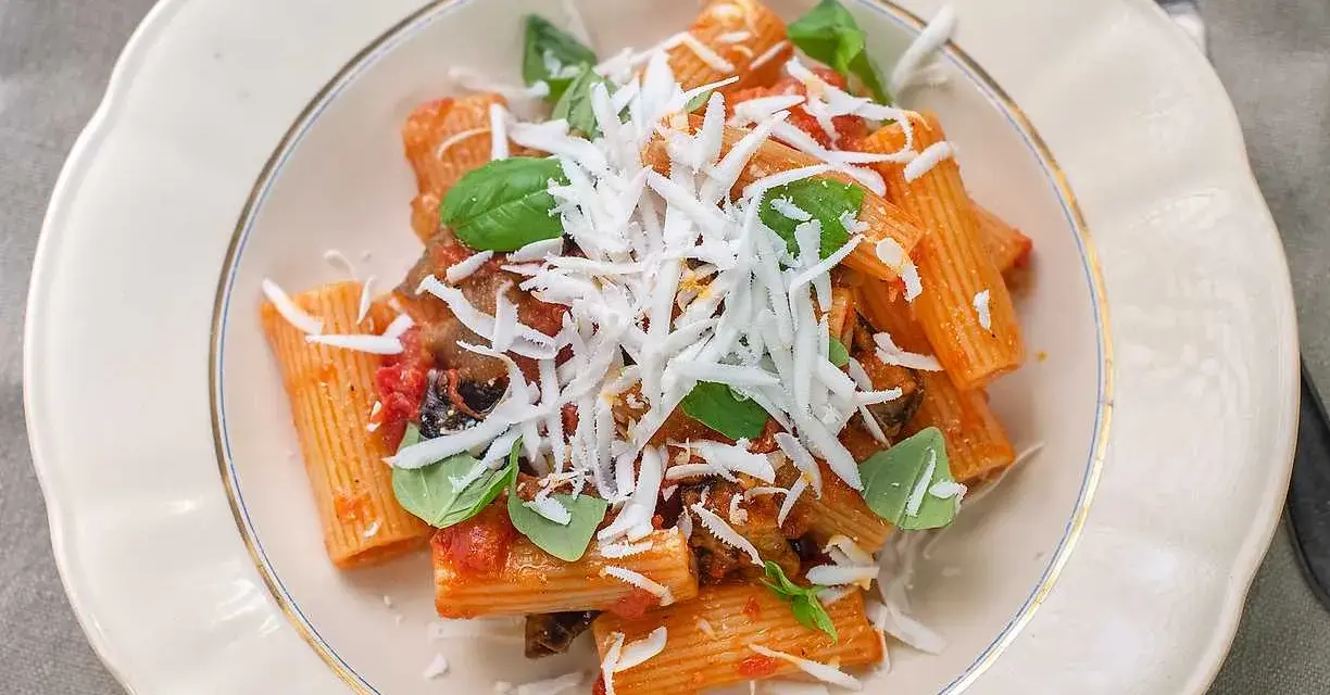 En tallrik med pasta alla norma, toppad med riven ost och färsk basilika.