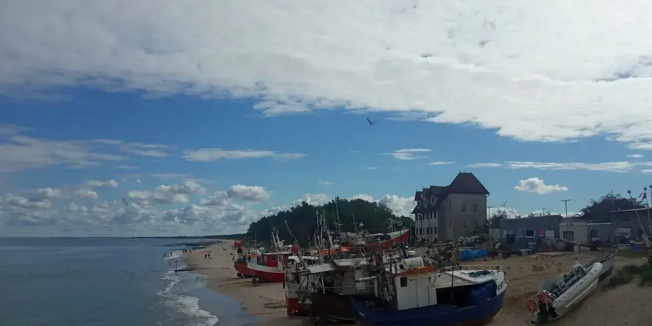 Chłopy trasa: łodzie rybackie na plaży, budynek z czerwonym dachem, morze i niebo z chmurami.