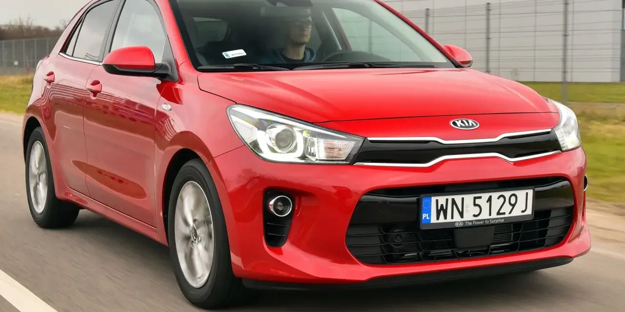 Czerwony Kia Rio w ruchu. Kierowca w okularach za kierownicą. Wiele pozytywnych kia rio opinie o tym modelu.
