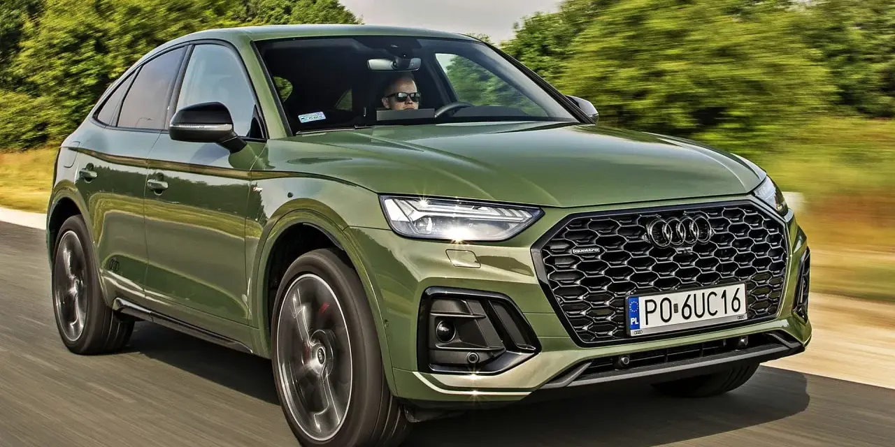 Zielone Audi Q5 Sportback z silnikiem 50 TFSI jedzie po drodze. Kierowca w okularach przeciwsłonecznych prowadzi auto.