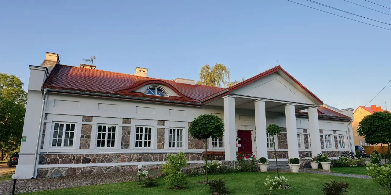 Elegancki pałac w Korczewie z kolumnowym portykiem i kamienną podmurówką, otoczony zadbanym ogrodem.
